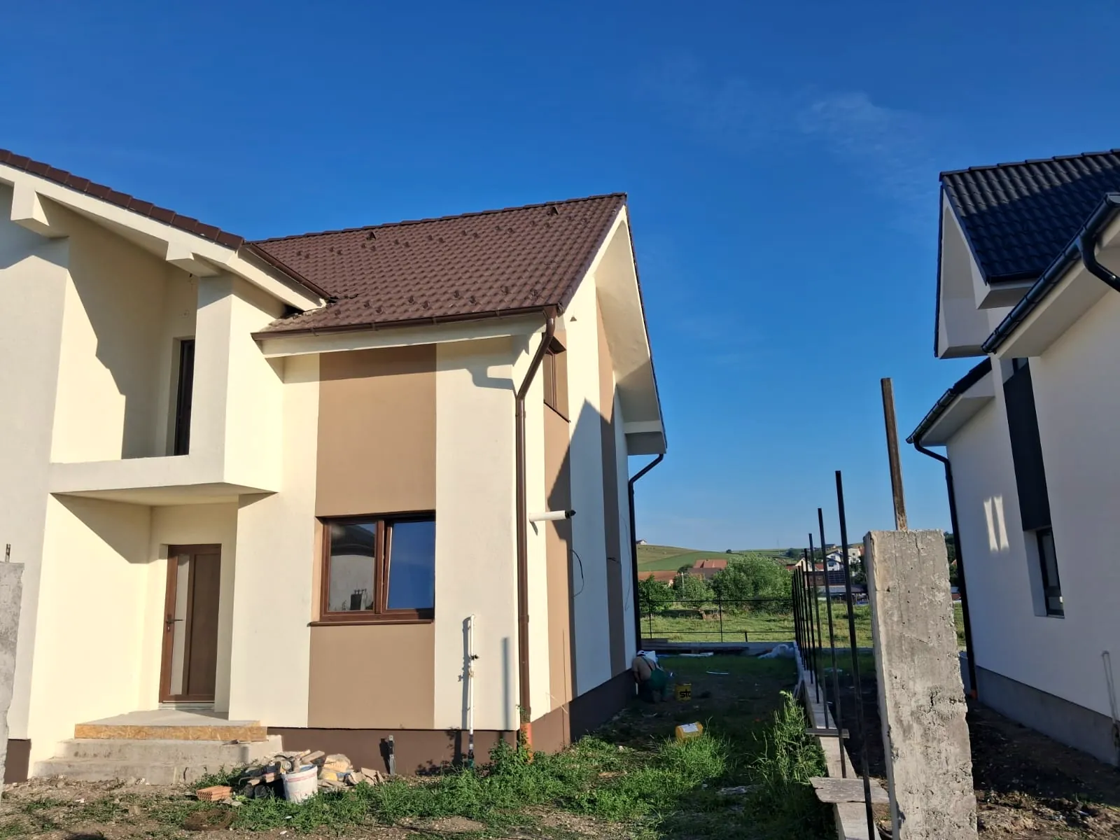 Casă cu etaj cu termosistem finalizat, tencuială crem și bej, văzută din lateral
